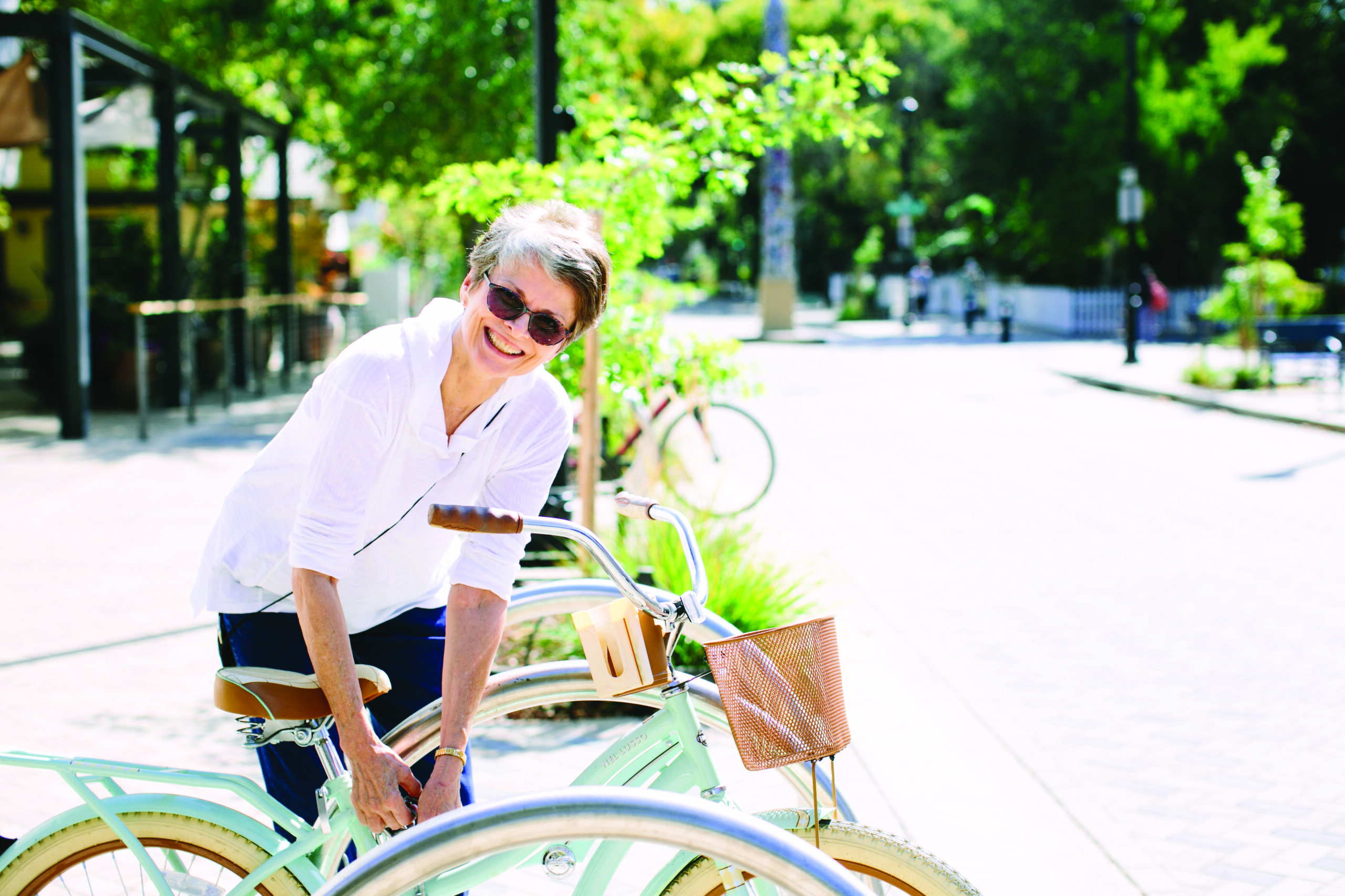 A woman wearing sunglasses smiles as she holds a bicycle